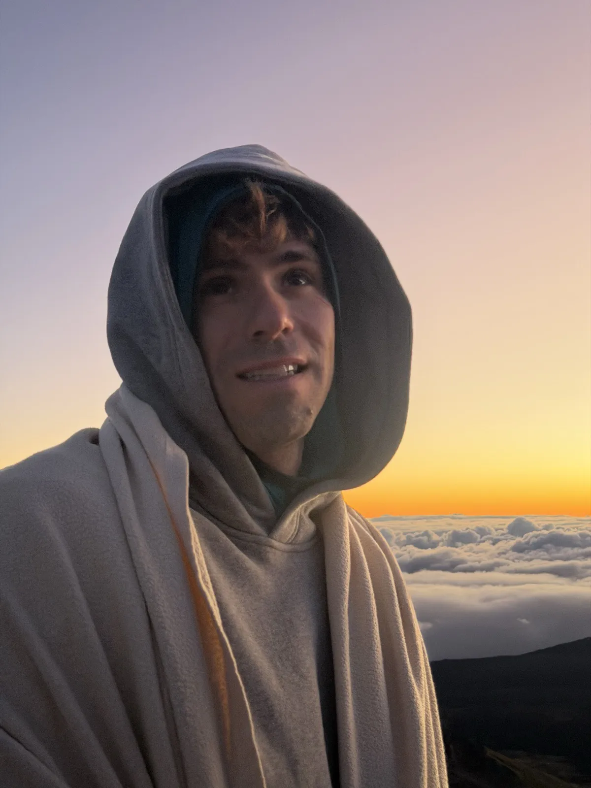 Nick in a hoodie above the clouds at sunrise